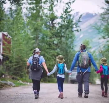 Family of four hiking on a mountain trail with backpacks and trekking poles